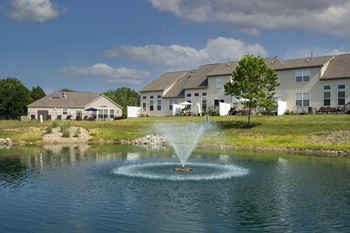 A fountain in the middle of a pond in front of a row of houses.